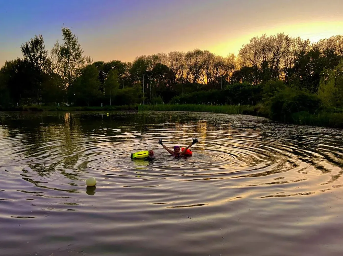 Two swimmers with tow floats sending ripples across the lake at sunset