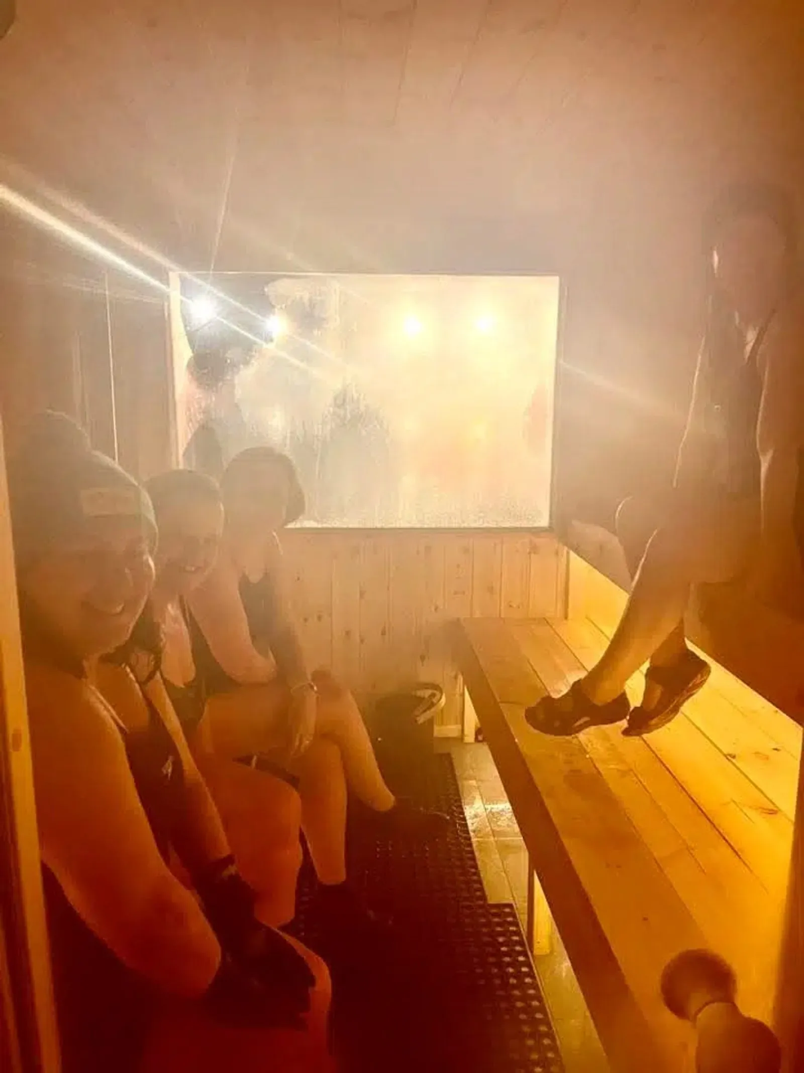 Steam glowing orange inside the sauna, with guests on the benches and a misted window