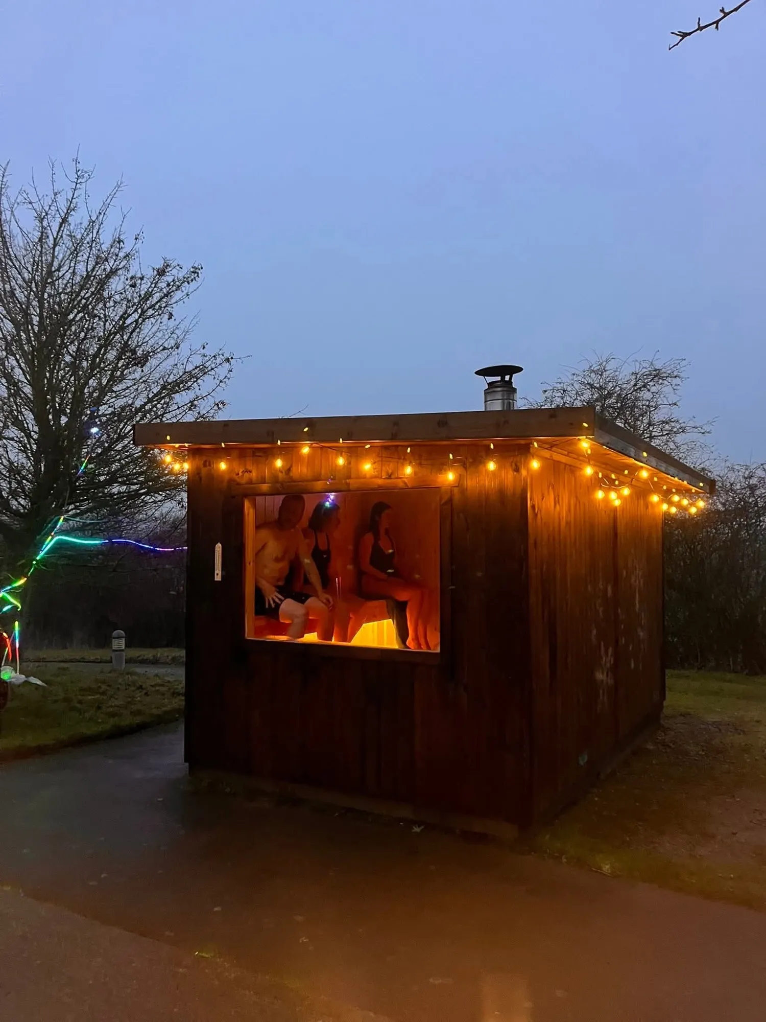 The sauna glowing at dusk with lights along its roof