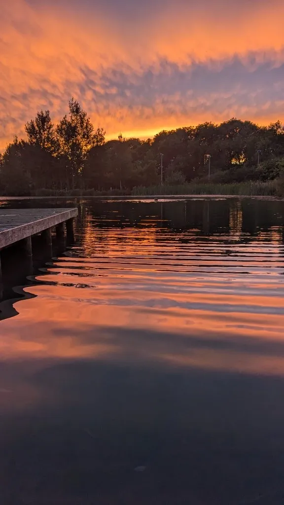 The jetty at sunset with an orange sky reflected in the still lake