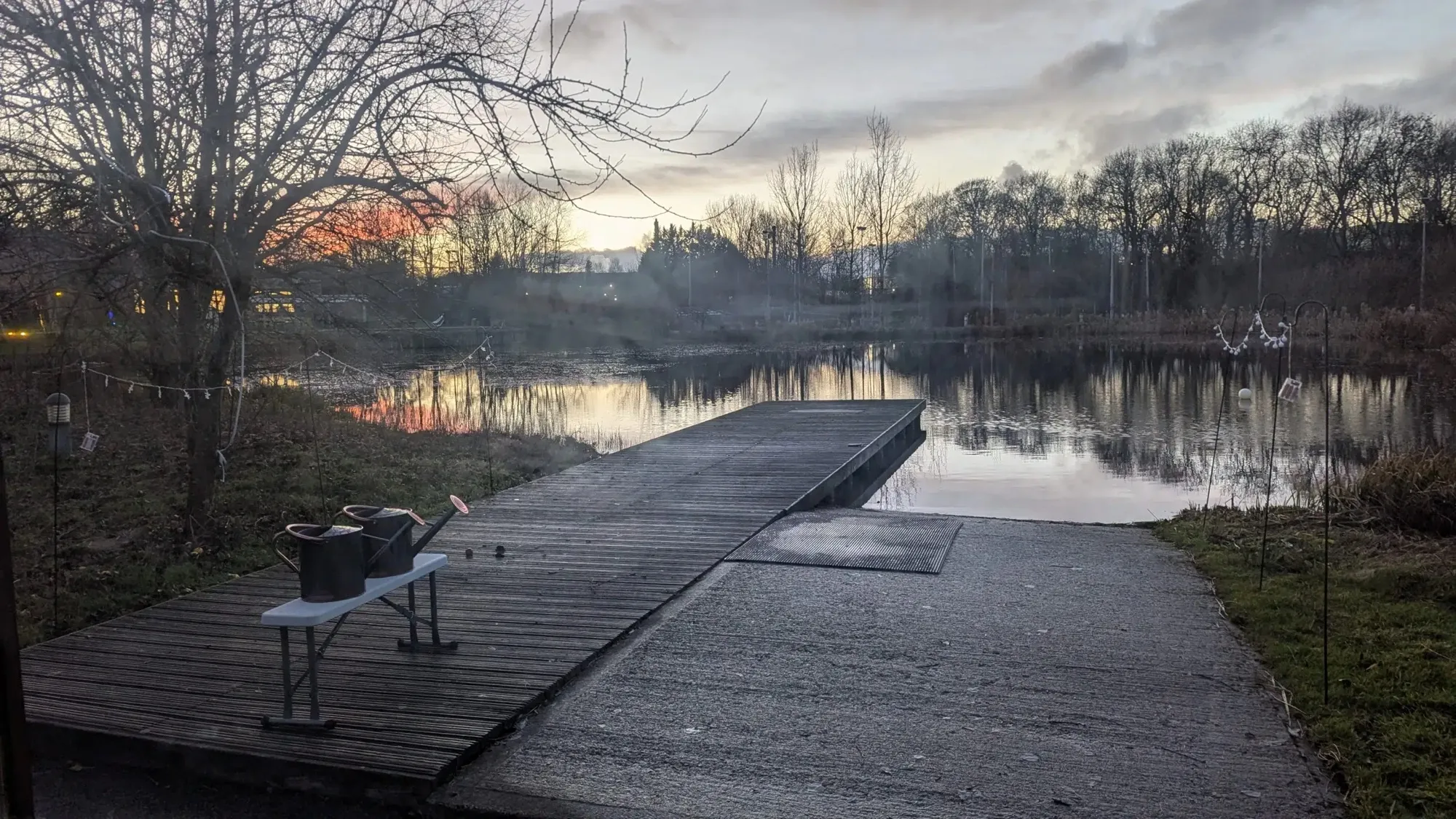 The frosted jetty stretching into the lake on a winter evening, watering cans on the bench