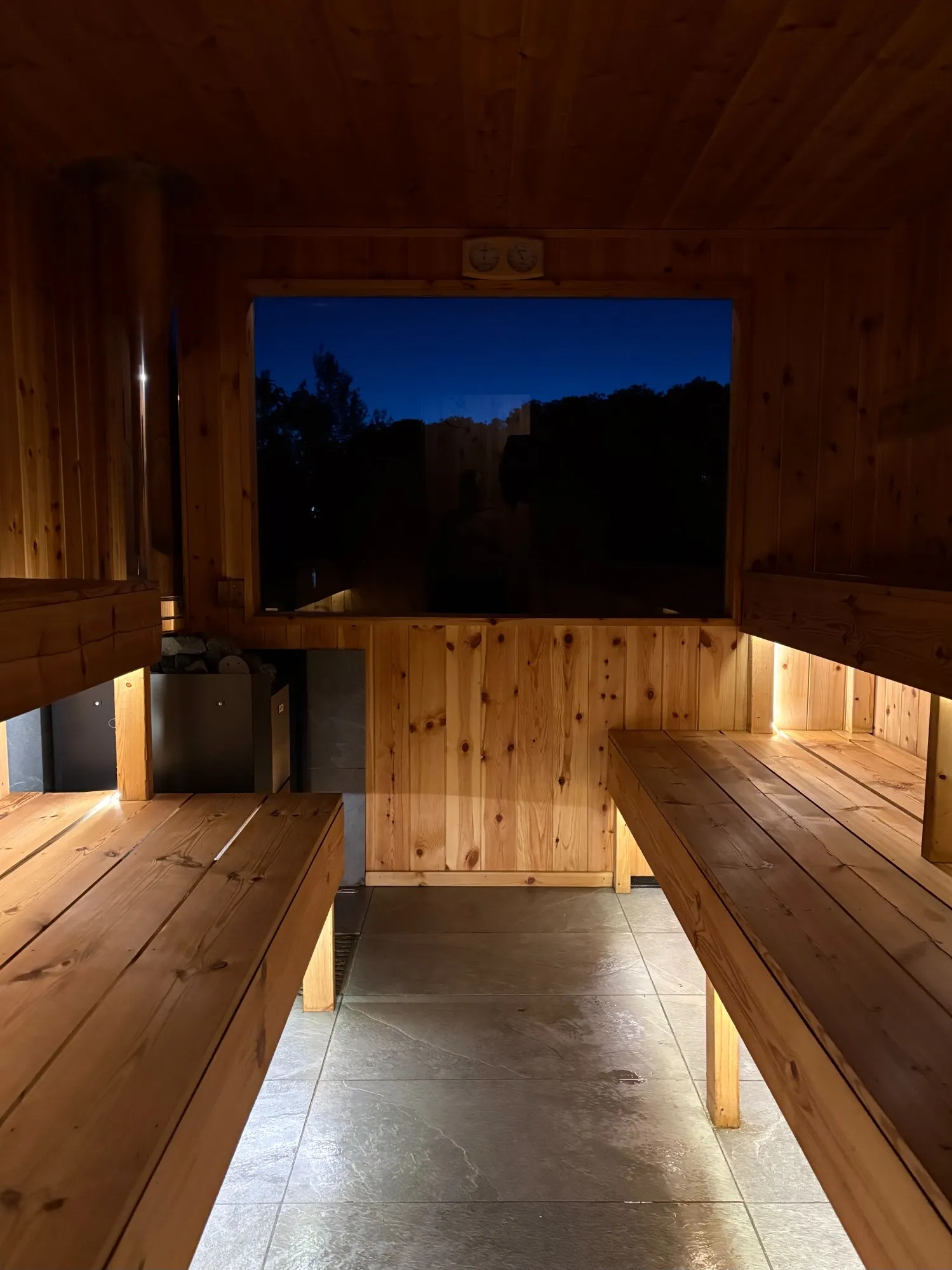 The sauna at dusk with soft lights under the benches and a deep-blue sky in the window