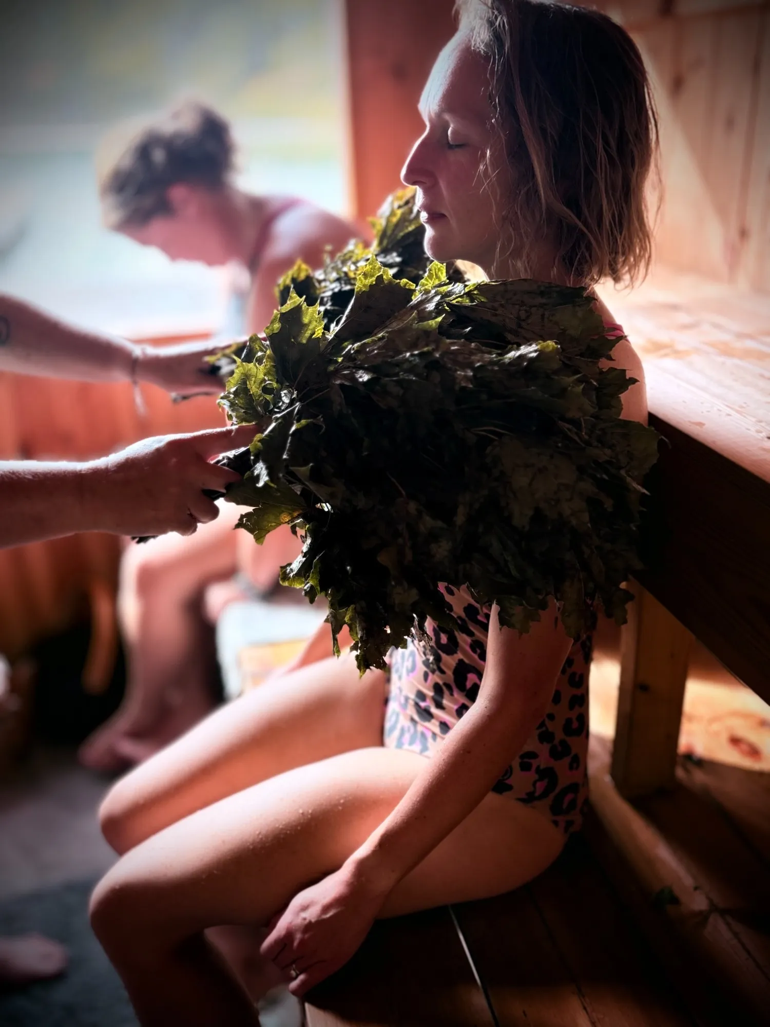 A guest with her eyes closed holding a leafy birch whisk during a guided sauna
