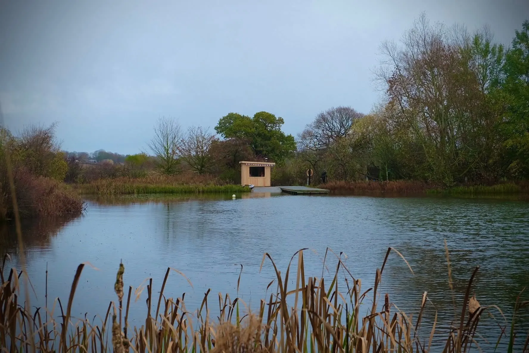 Looking across the lake to the small wooden sauna and jetty on a grey autumn day