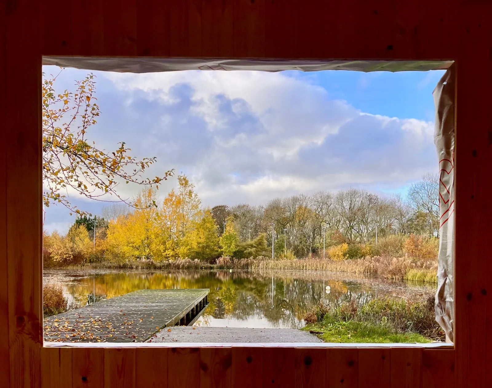 Autumn view of the lake and the wooden jetty, framed by the sauna window