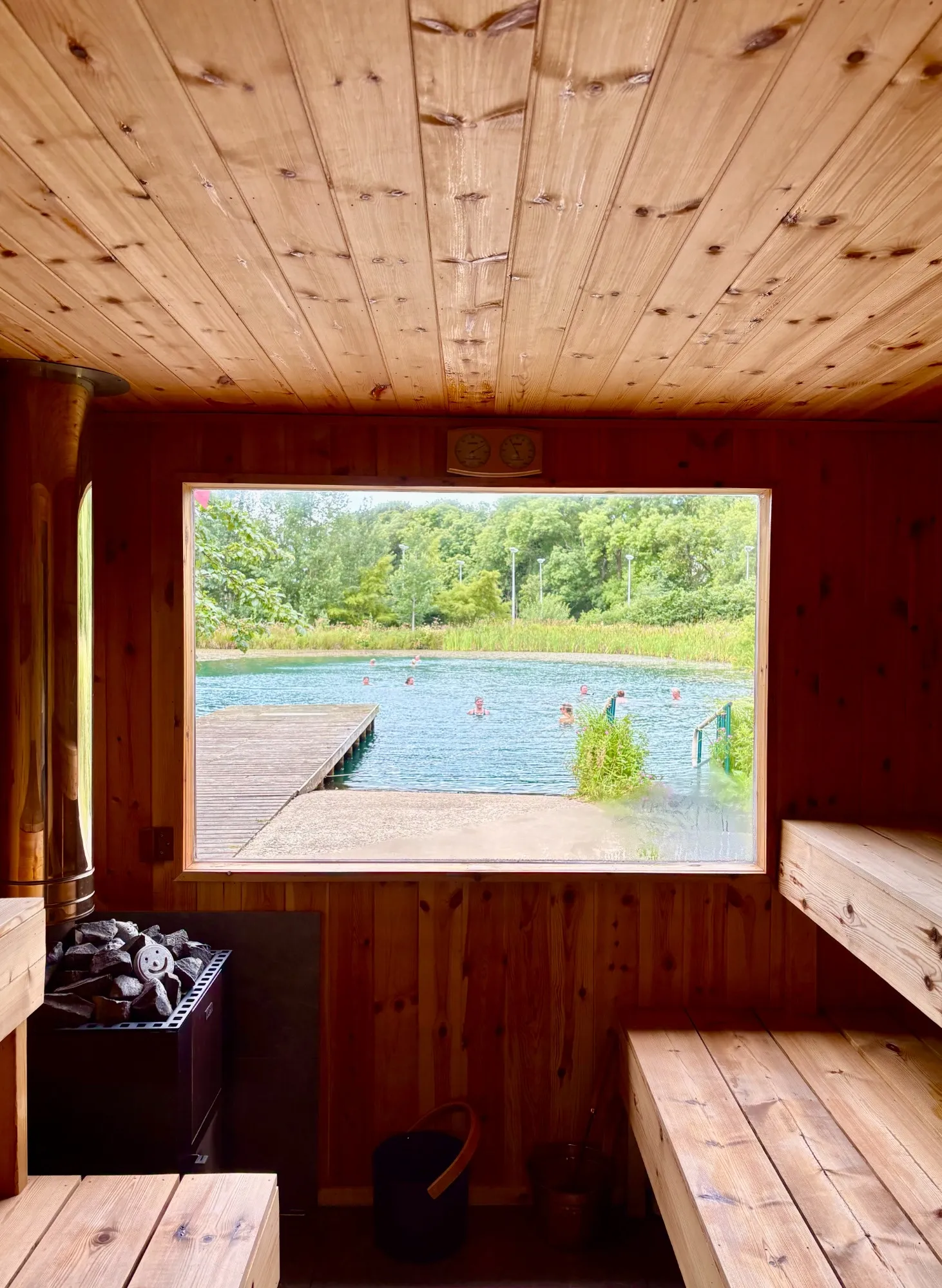 Inside the sauna on a summer day, with swimmers and the jetty visible through the window