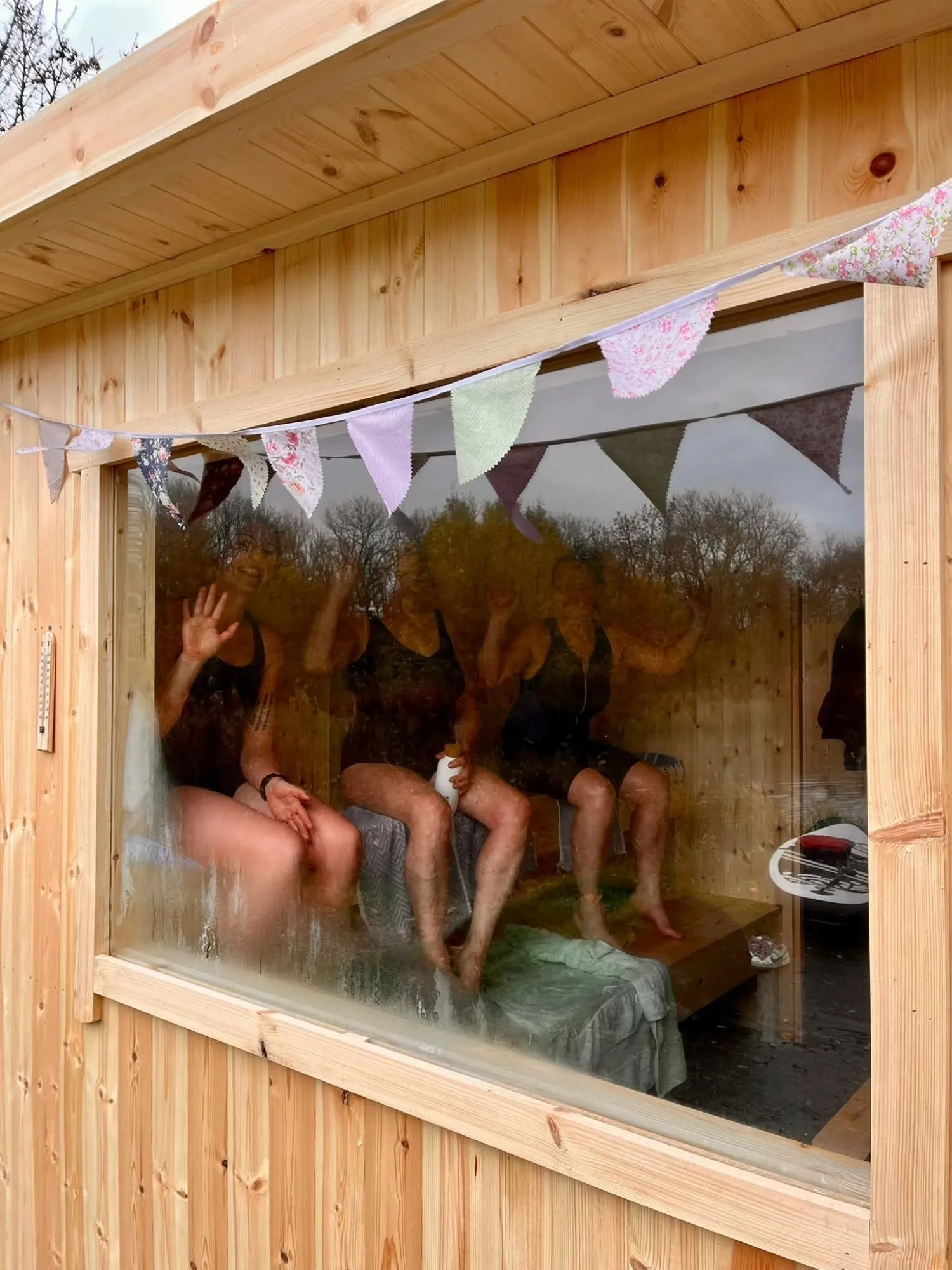 Guests waving through the sauna window, with bunting along the timber outside